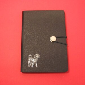 Può includere: Diario in pelle nera con chiusura a bottone argentato e design a silhouette di cane argentato.