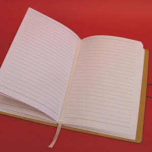 May include: A brown leather-bound journal with a white ribbon bookmark and lined pages. The journal is open to a blank page.