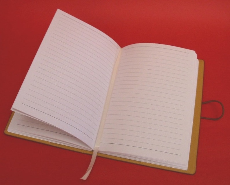 May include: A brown leather-bound journal with a white ribbon bookmark and lined pages. The journal is open to a blank page.