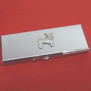 May include: A rectangular silver-toned metal case with a polished, reflective surface. Centered on the lid is a raised, three-dimensional pewter-coloured emblem depicting a Highland cow with long, shaggy fur and prominent horns.