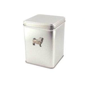 May include: A silver-coloured, rectangular metal tin with a matching lid. A small, detailed pug dog emblem is affixed to the front. The tin is designed for storage and has a simple, clean aesthetic.