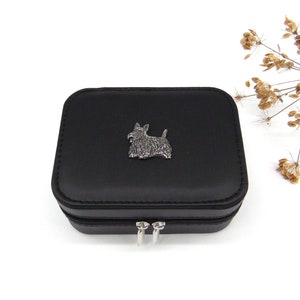 Könnte beinhalten: Schwarze Schmuckschatulle mit einem silbernen Schotten-Hunde-Anhänger auf dem Deckel. Die Box hat einen Reißverschluss.