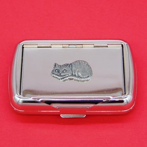 Puede incluir: Una caja de cigarrillos de metal plateado con un diseño de gato de peltre en la parte delantera.
