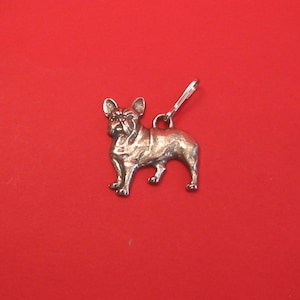 May include: Silver charm of a French Bulldog standing on a red background.