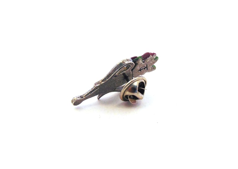 May include: A silver pin with a red, green, and white flower design. The pin has a safety clasp on the back.