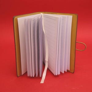 K&ouml;nnte beinhalten: Ein braunes, ledergebundenes Tagebuch mit einem wei&szlig;en Satinband als Lesezeichen. Das Tagebuch ist ge&ouml;ffnet und zeigt linierte Seiten.