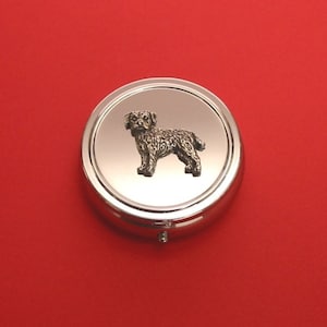 May include: A silver round pill box with a small, detailed, pewter image of a brown and black terrier dog on the lid.