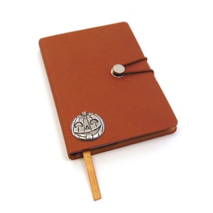 May include: A brown leather journal with a silver pumpkin charm and a brown ribbon bookmark.