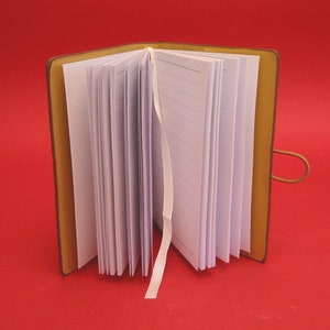 May include: A brown leather-bound journal with a white ribbon bookmark. The journal has lined pages and is open to reveal the blank pages.