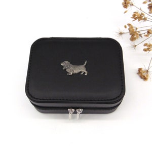 Puede incluir: Caja de joyería negra con un diseño de perro sabueso basset plateado en la tapa. La caja tiene un cierre de cremallera.