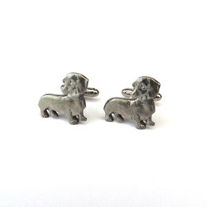 Puede incluir: Un par de gemelos de plata con forma de dachshund. Los gemelos son detallados y realistas.