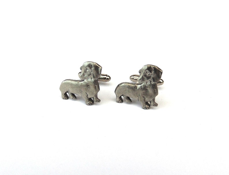 Puede incluir: Un par de gemelos de plata con forma de dachshund. Los gemelos son detallados y realistas.