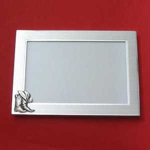 May include: A silver picture frame with a boot and hat design on the bottom right corner.