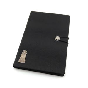 May include: A black leather journal with a silver lighthouse charm and a silver button closure. The journal has a black elastic band.