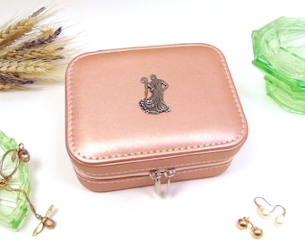 Puede incluir: Una caja de joyería de color oro rosa con cierre de cremallera. La caja tiene un diseño de metal plateado de una pareja bailando en la parte superior.