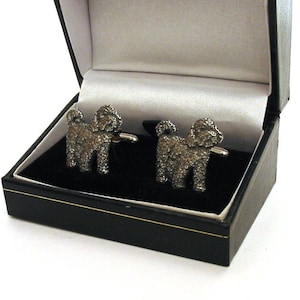 May include: A pair of silver cufflinks in a black box. The cufflinks are shaped like poodles.