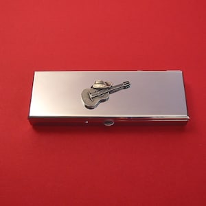 May include: A silver metal pill box with a small, detailed guitar design on the lid.