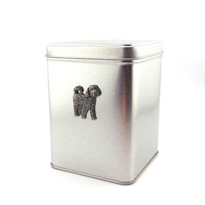 May include: A silver metal tin with a black and white dog silhouette on the front. The tin is square shaped and has a smooth surface.