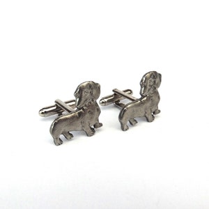 Puede incluir: Un par de gemelos de plata con forma de dachshund. Los gemelos son detallados y realistas.