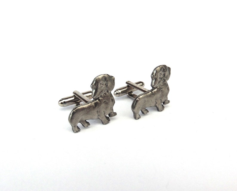 Puede incluir: Un par de gemelos de plata con forma de dachshund. Los gemelos son detallados y realistas.
