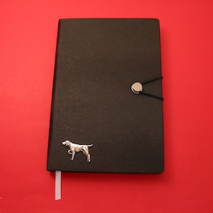 May include: A black leather journal with a silver dog silhouette and a silver button closure. The journal has a white ribbon bookmark.