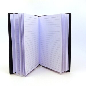 May include: A black leather-bound journal with lined pages is open to a blank page. The journal is closed on the left side and open on the right side.