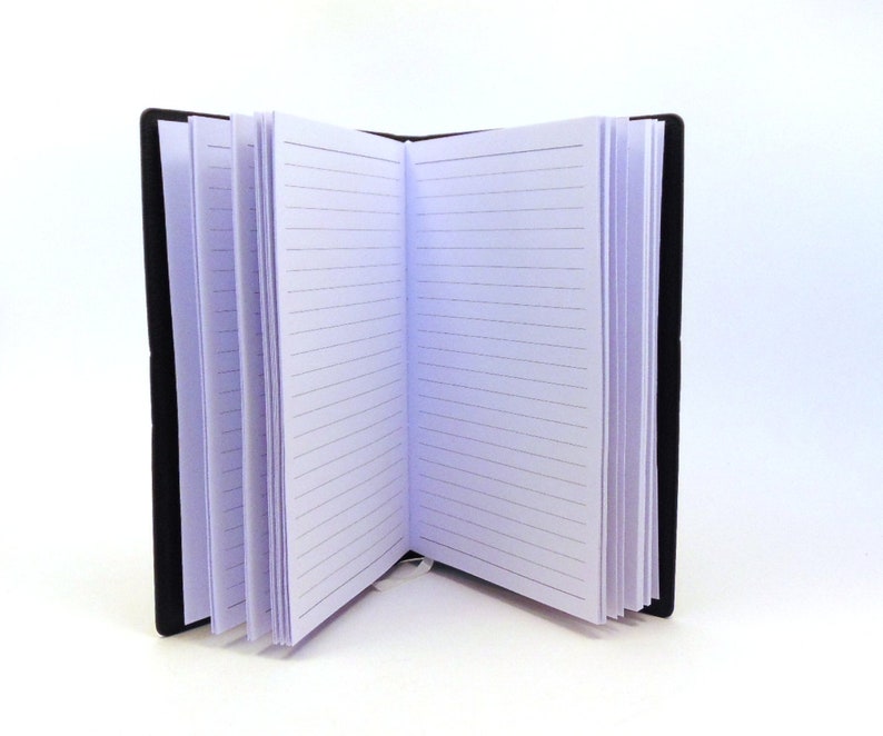 May include: A black leather-bound journal with lined pages is open to a blank page. The journal is closed on the left side and open on the right side.