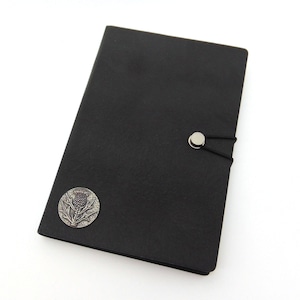 May include: Black leather journal with a silver thistle emblem and an elastic closure.