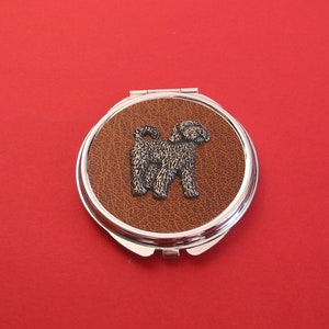 May include: A silver compact mirror with a brown leatherette cover featuring a silver 3D image of a dog.
