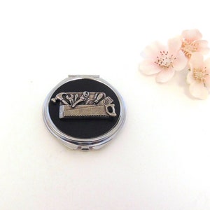 May include: A silver compact mirror with a black background and a silver 3D image of a toolbox with tools inside.