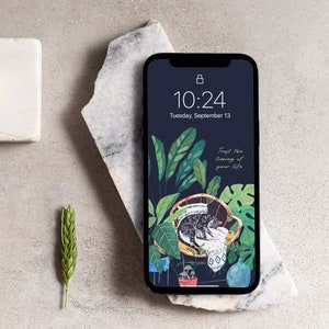 May include: A phone screen displaying a dark blue background with a green and white illustration of a cat sleeping in a wicker chair surrounded by plants. The time is 10:24 and the date is Tuesday, September 13. The text "Trust the timing of your life" is displayed on the screen.