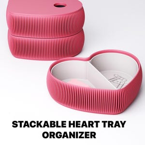 May include: Pink stackable heart-shaped tray organizer. The organizer has a ribbed exterior and a divided interior. The top tray has a hole. The text "STACKABLE HEART TRAY ORGANIZER" is displayed below the trays.