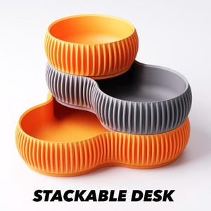 May include: Stackable desk organizers in orange and gray. The organizers have a ribbed design and are stacked in a three-tiered configuration. The text "STACKABLE DESK ORGANIZERS" is at the bottom of the image.