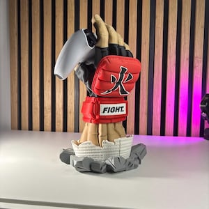 May include: A sculpted hand wearing a red and black fingerless fighting glove with the Japanese kanji for fire and a red wrist strap labeled FIGHT. The hand holds a white gaming controller and emerges from a base of cracked white and gray stone.
