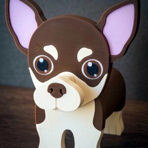 May include: A wooden chihuahua dog figurine with a brown body, white face, and large, expressive eyes. The dog has pink inner ears and is standing on a wooden surface. The figurine is a decorative item.