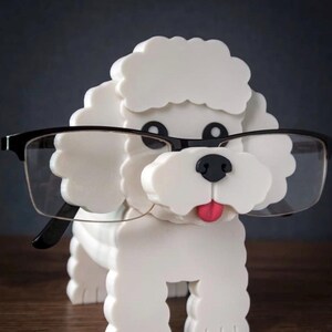 May include: A white dog-shaped eyeglasses holder with black-rimmed glasses. The dog has a pink tongue and black eyes and nose. The holder is made of a solid material and is designed to hold eyeglasses.
