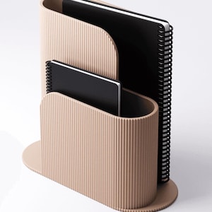 May include: A beige desk organizer with a ribbed texture, holding two black spiral-bound notebooks. The organizer has a curved design with a rounded base, providing a stylish storage solution for office or home use.