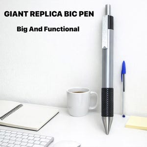 K&ouml;nnte beinhalten: Ein riesiger BIC-Stift-Nachbau mit silbernem Geh&auml;use, schwarzer, strukturierter Griffzone und silbernem Clip, platziert neben einem blauen Standard-Kugelschreiber. Der Text GIANT REPLICA BIC PEN Big And Functional ist oben links zu sehen.