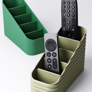 May include: Two remote control organizers in shades of green. One is a solid, bright green with four compartments. The other is a lighter green with a ribbed design, holding two remote controls. The remotes are black and gray.