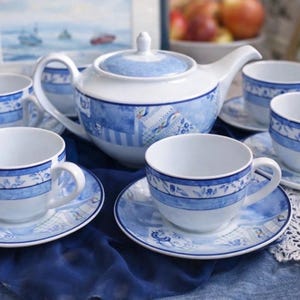 Op de afbeelding: Een wit porseleinen theeservies met blauwe bloemen- en geometrische patronen. De set bevat een theepot, zes kopjes en schotels. De kopjes en schotels zijn rond de theepot gerangschikt.