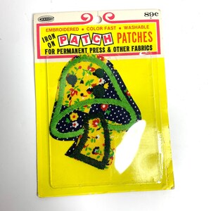 May include: A colorful iron-on patch in a mushroom shape, featuring a yellow floral pattern, navy blue polka dots, and green trim. The patch is packaged on a yellow backing with text that reads "IRON ON PATCH PATCHES".