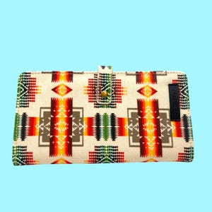 May include: Cream-colored wallet with a Southwestern-inspired geometric pattern in red, orange, yellow, green, and brown. The wallet has a snap closure and a black label that reads "PENDLETON".