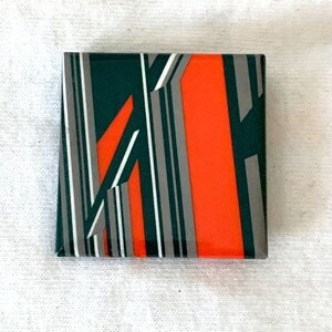 May include: Square decorative tile with an abstract design. The tile features a vibrant orange rectangle, dark green sections, and vertical stripes in gray and white. The design is geometric and modern.