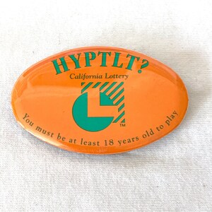 Pode incluir: Pin oval laranja com o texto verde "HYPTLT? California Lottery". O pin apresenta um logotipo "L" verde e o texto "You must be at least 18 years old to play."