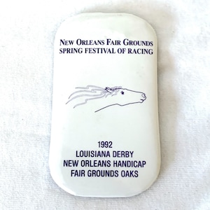 May include: A white rectangular souvenir with blue text and a horse illustration. The text reads "New Orleans Fair Grounds Spring Festival of Racing" and "1992 Louisiana Derby".
