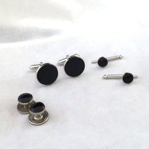 May include: A set of formalwear accessories, including cufflinks, shirt studs, and collar stays. The cufflinks and shirt studs have a round, black center with a silver-colored metal backing. The collar stays also have a black center.