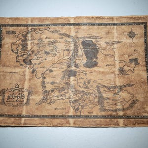 May include: A detailed map of a fantasy world, printed on aged parchment. The map features intricate illustrations of landscapes, mountains, and rivers, with a decorative border and text in a stylized font. The color palette is primarily brown and black.