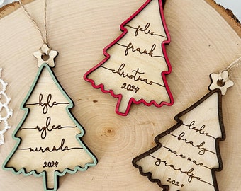 May include: Three wooden Christmas tree ornaments with names and the year 2023 inscribed on them. The ornaments are painted in red, green, and brown.