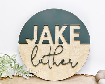 May include: A round wooden sign with a green half circle on top. The name "JAKE LUTHER" is written in green on the sign.