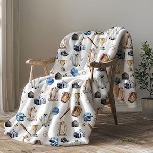 May include: White fleece throw blanket with a repeating pattern of baseball equipment, including bats, gloves, jerseys, and baseballs. The pattern is in shades of blue, brown, and gold. The blanket is draped over a wooden chair.